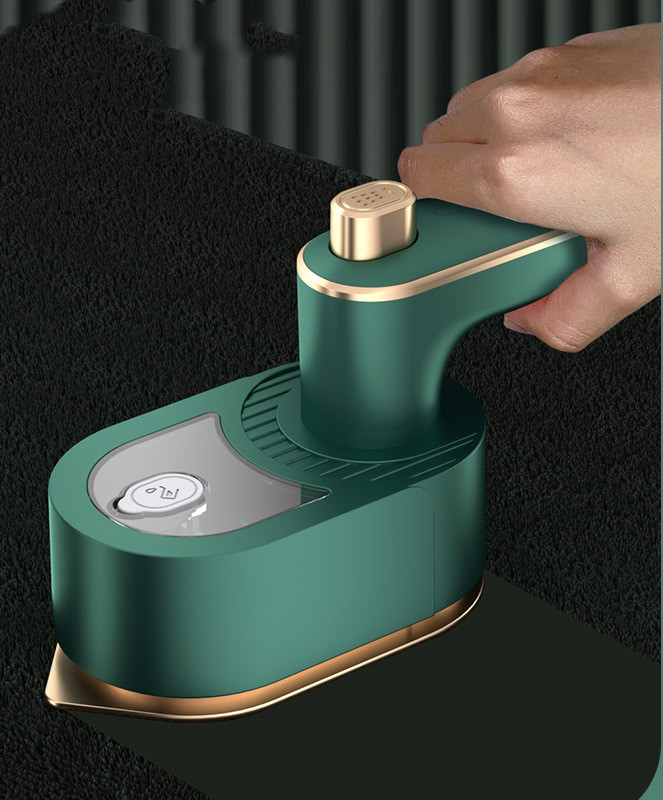 Hand gliding the green mini steam iron over dark fabric